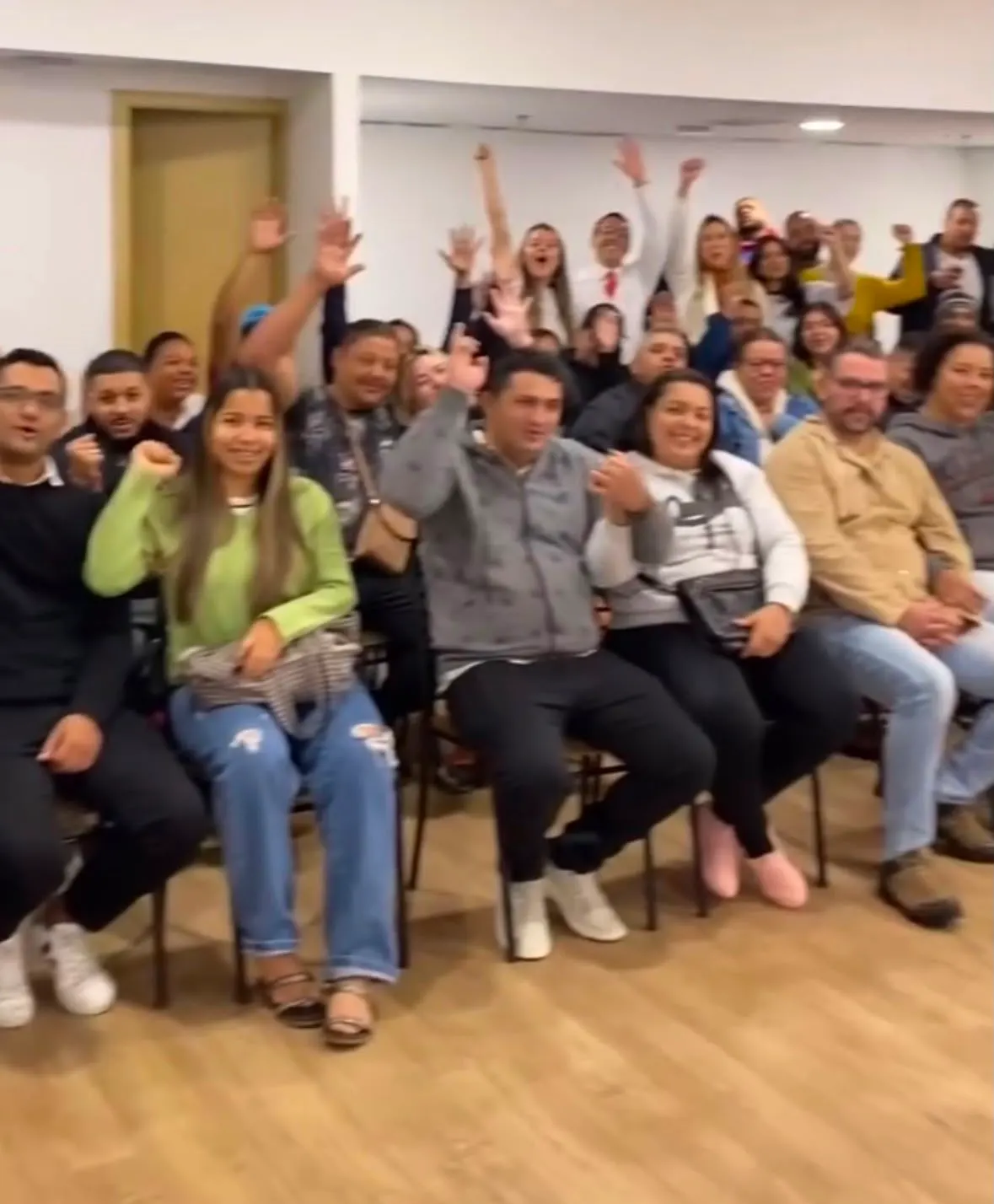 Plateia sentada em cadeiras comemora com os braços levantados durante o encontro.