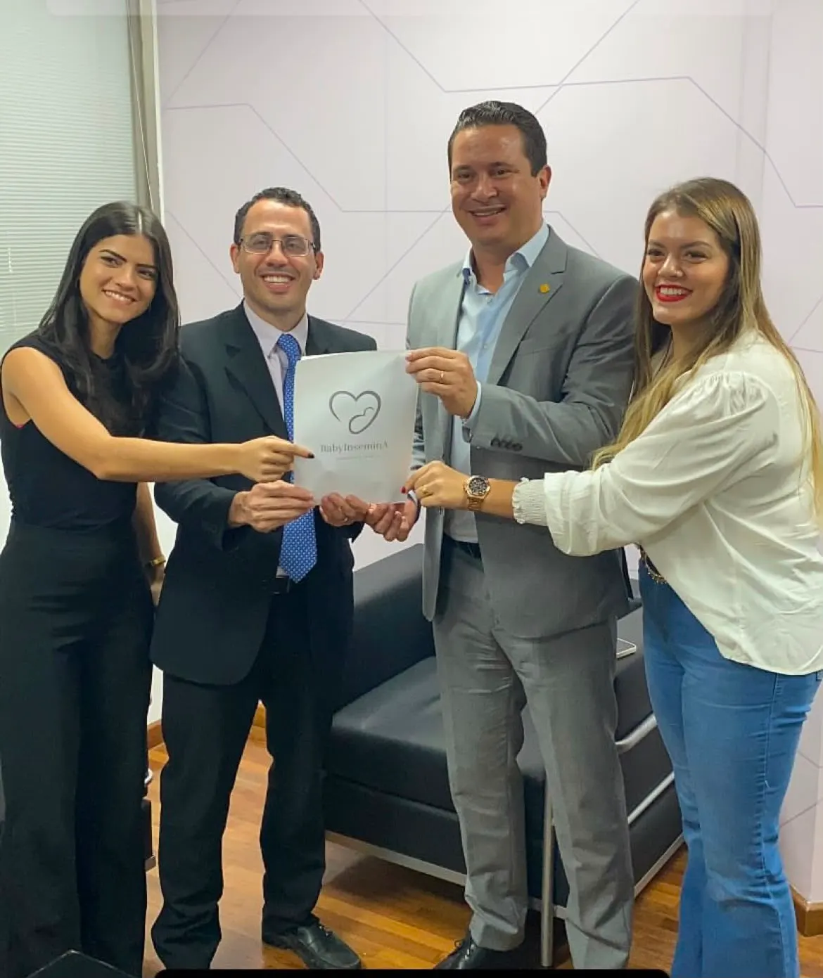 Quatro pessoas seguram juntas uma pasta com a marca Baby InseminA durante reunião institucional.